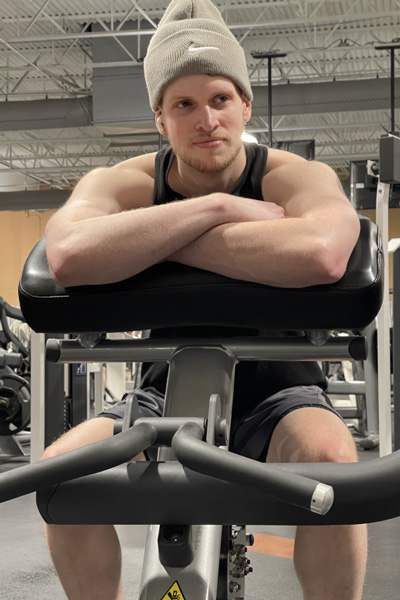 Doug Volker sitting on a bicep curl machine with his arms folded.